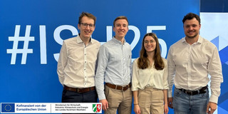 Vier Menschen vor einem Werbebanner einer Messe