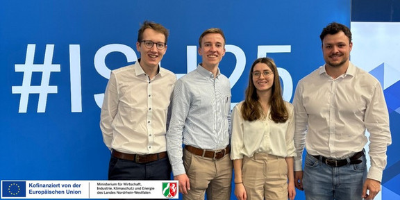 Vier Menschen vor einem Werbebanner einer Messe